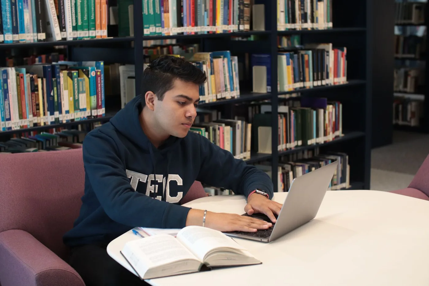 Student using a laptop with books open on a library desk