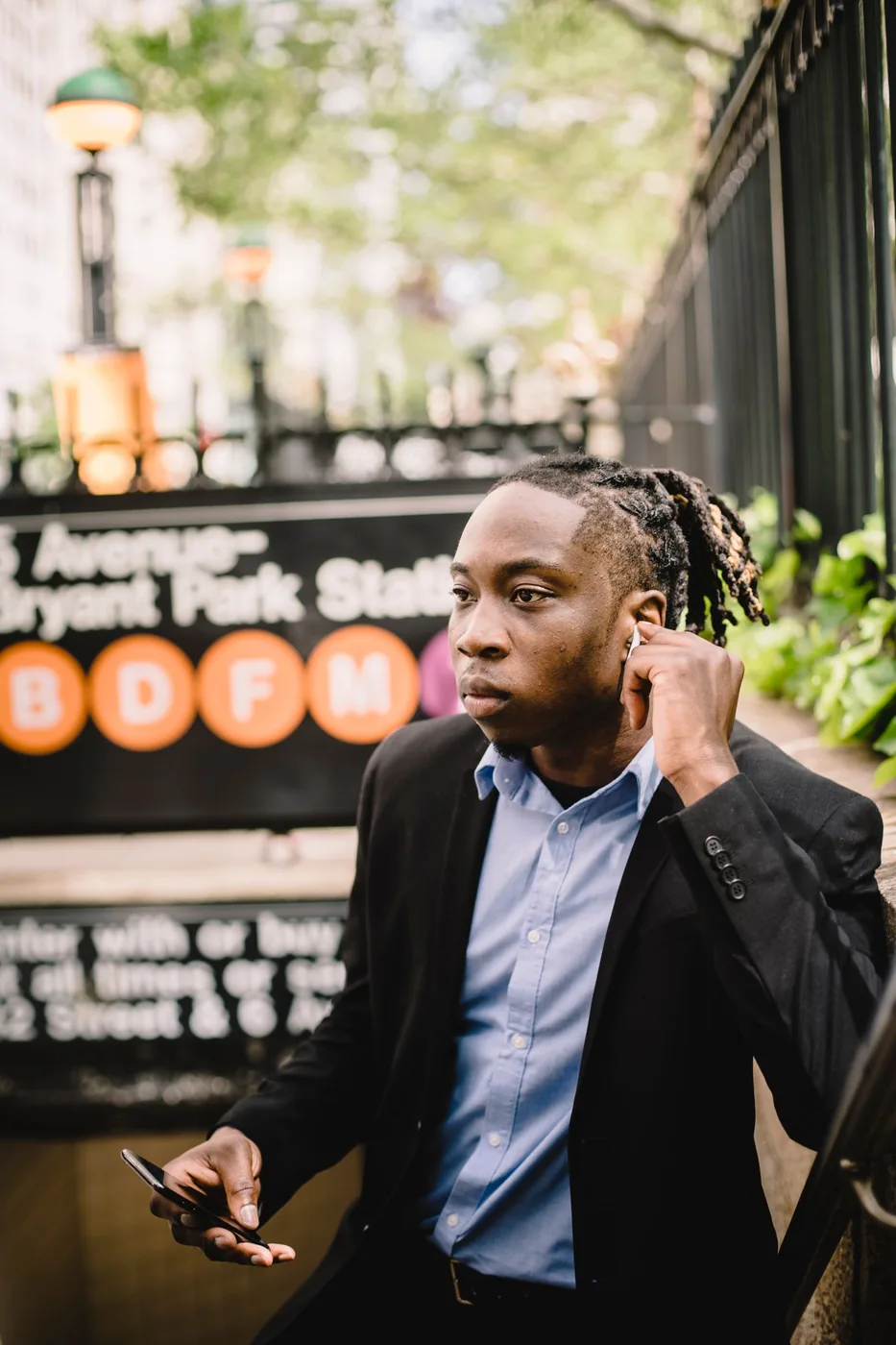 Man wearing earbuds and a suit beside the steps of a subway entrance