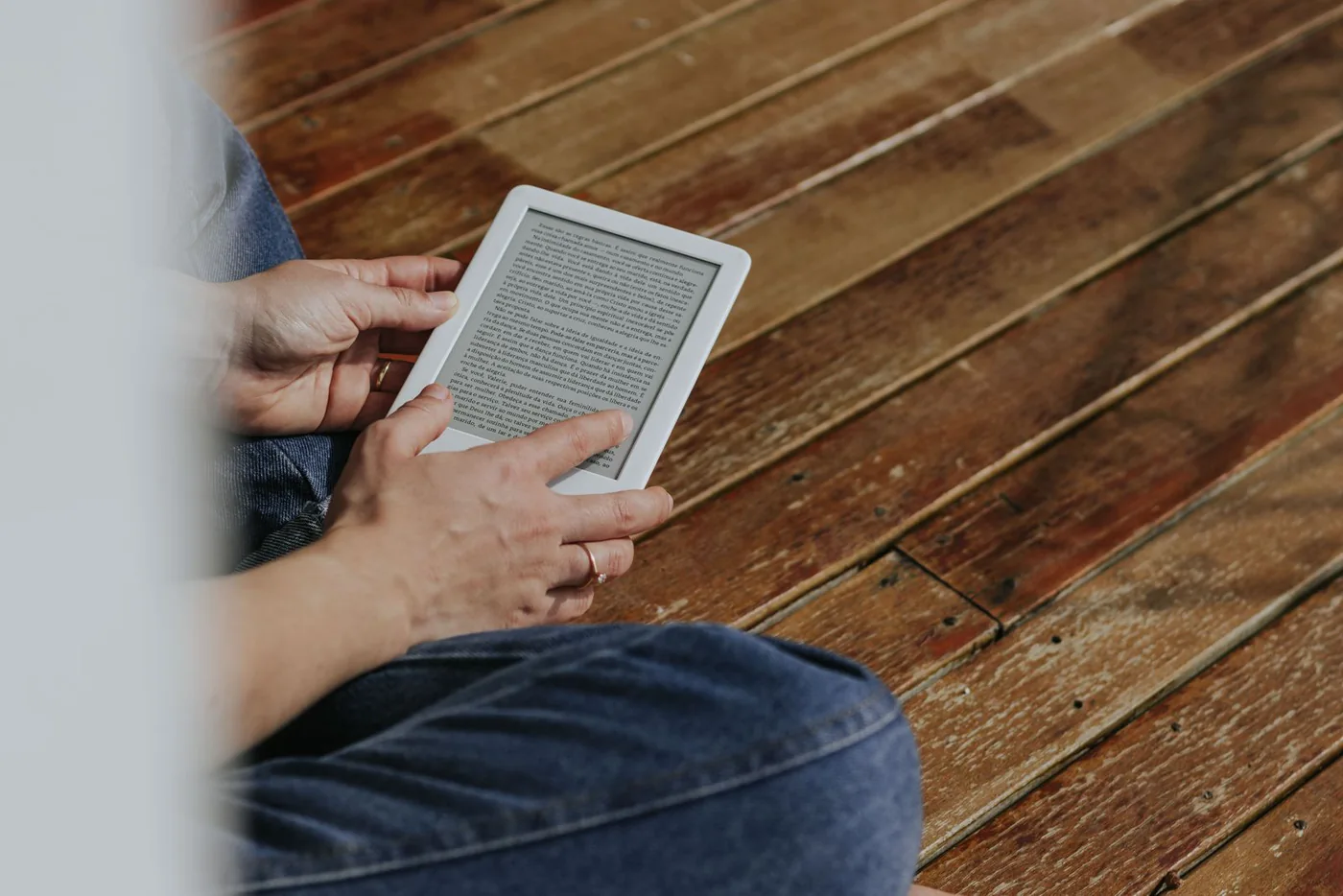 Hands holding an e-reader while sitting on a wooden floor